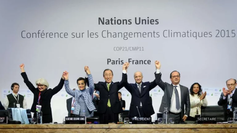 Delegados das Nações Unidas celebram de mãos erguidas a aprovação do Acordo de Paris durante a COP21 em 2015, em França.