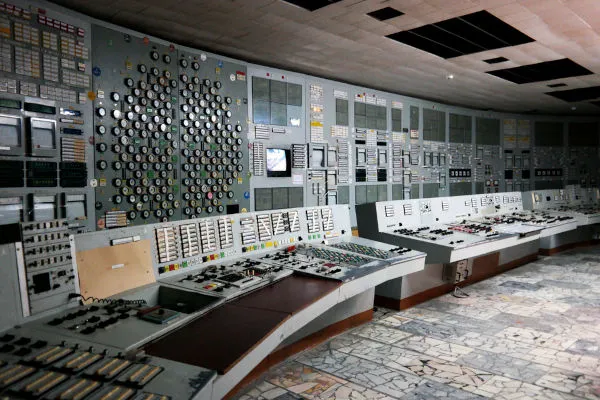 Sala de controlo abandonada do reator 4 da usina nuclear de Chernobyl, com painéis enferrujados, botões quebrados e instrumentos destruídos.